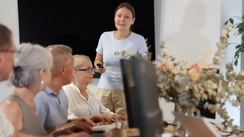 Middle-aged female instructor teaching computer skills to old students during IT Video stock 271253634