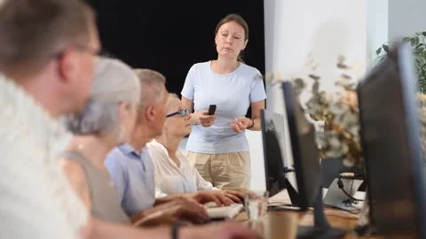 Middle-aged female instructor teaching computer skills to old students during IT Stock Footage 310963433