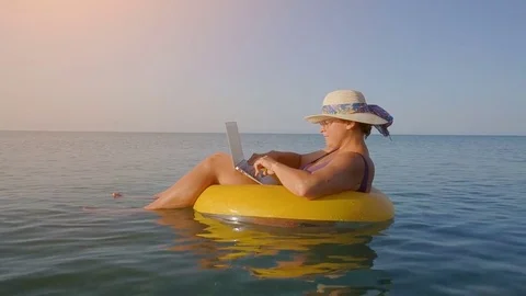 Middle aged female working on laptop computer in orange inflatable life ring Stock Footage 80567335