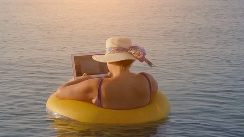 Middle aged female working on laptop computer in orange inflatable life ring Stock Footage 80567344