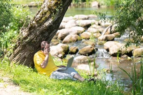 Middle aged freelancer using a laptop computer and phone while working in bea Foto stock