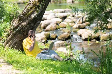 Middle aged freelancer using a laptop computer and phone while working in bea Stock Photos