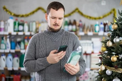 Middle-aged guy scanning QR-code on dishwashing liquid in store with New Year Stock Photos