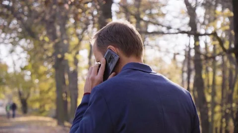 A middle-aged handsome Caucasian man talks on a smartphone as he walks in a park Stock Footage 201780382