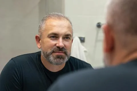 Middle-aged handsome man looking in mirror in bathroom Stock Photos