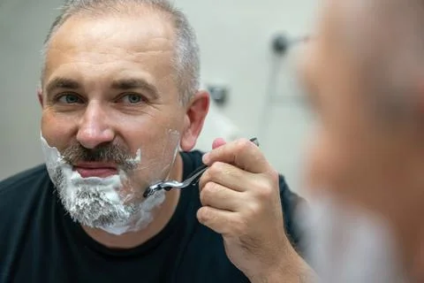 Middle aged handsome man shaving his beard in bathroom Stock Photos
