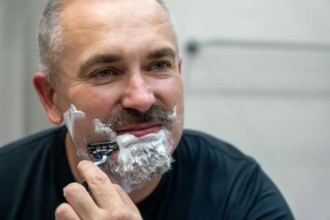 Middle aged handsome man shaving his beard in bathroom Stock Photos
