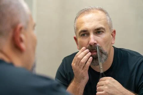 Middle-aged handsome man using scissors to cut his beard a litlie and fix the Stock Photos