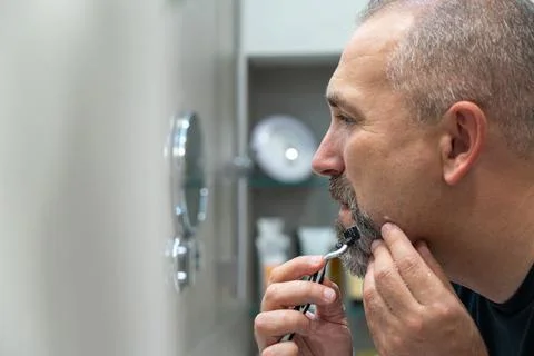 Middle-aged handsome man using razor in bathroom Foto stock