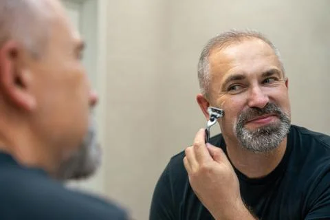 Middle-aged handsome man using razor in bathroom Stock Photos