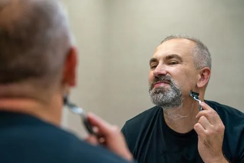 Middle-aged handsome man using razor in bathroom Foto stock