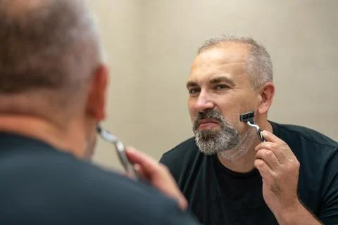 Middle-aged handsome man using razor in bathroom Stock Photos