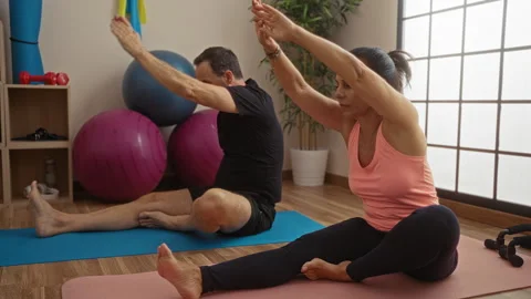 Middle-aged hispanic couple exercising indoors on yoga mats at gym with fit.. Stock Footage 303417171