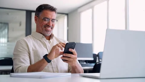 Middle aged Hispanic manager ceo businessman using cell phone mobile app, laptop Stock Footage 241689619