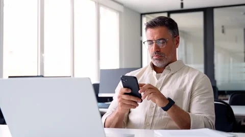 Middle aged Hispanic manager ceo businessman using cell phone mobile app, laptop Stock Footage 241689675