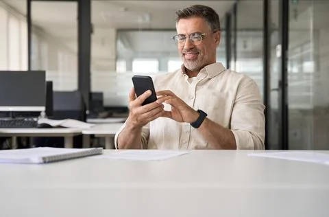 Middle aged Hispanic manager ceo businessman using cell phone mobile app, laptop Stock Photos