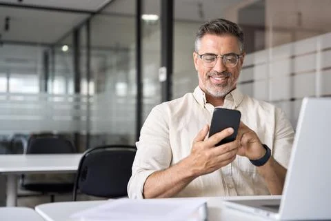 Middle aged Hispanic manager ceo businessman using cell phone mobile app, laptop Stock Photos
