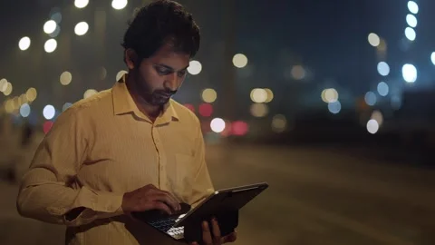 A middle aged Indian man typing on a laptop in the city outdoors night Stock Footage 330955201