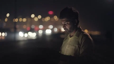 A middle aged Indian man using digital tablet with night traffic moving in back Stock Footage 330885577