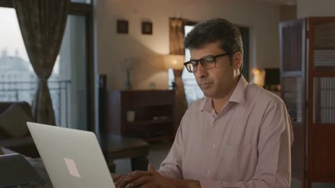 Middle aged Indian Man working remotely using a laptop looking at camera smiling Stock Footage 176779996
