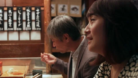Middle aged Japanese couple using chopsticks to eat sushi while chef talks in sm Stock Footage 199459483