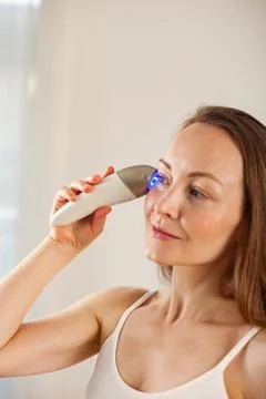 Middle aged lady doing led therapy facial massage using anti-aging electric m 写真素材