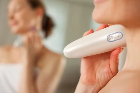 Middle aged lady doing led therapy neck skin care massage using anti-aging el Foto stock