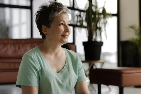 A middle aged lady enjoys rest at home. A woman with soft kindly smile sits Stock Photos