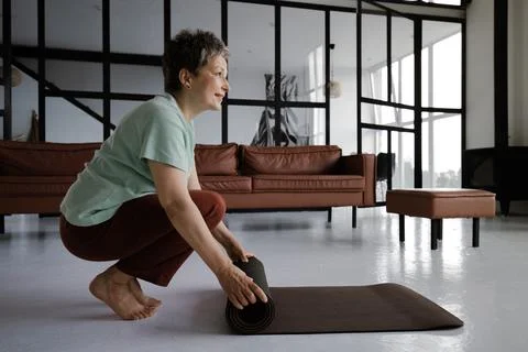 A middle aged lady practices yoga at home. A smiling woman in a satisfied mood Stock Photos