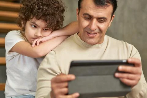 Middle aged latin father using tablet pc while spending time together with his Stock Photos