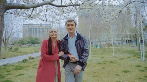 A middle-aged loving couple approaches a tree in the park and talks Stock Footage 129502904
