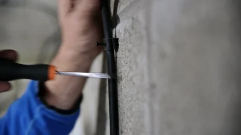 Middle aged Male hands using a screw driver to hold wire on wall with clip in Stock Footage 141862104