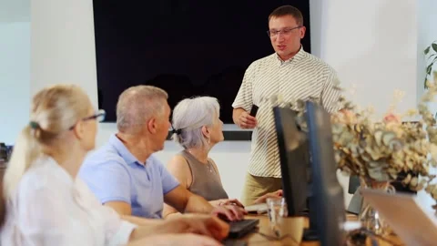 Middle-aged male instructor teaching computer skills to old students during IT Video stock 256619253