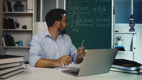Middle-aged male math tutor explaining lesson on chalkboard during video class Stock Footage 311461927