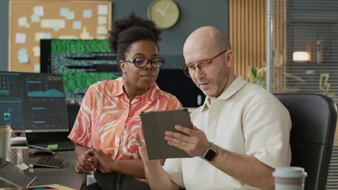 Middle-Aged Male Programmer Asking Younger Colleague for Help with Coding Stock Footage 306847951