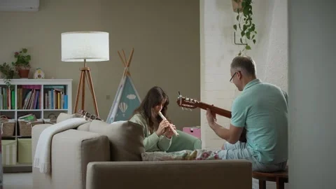 A middle-aged man and a 12-year-old girl playing guitar and a recorder Stock Footage 318783906
