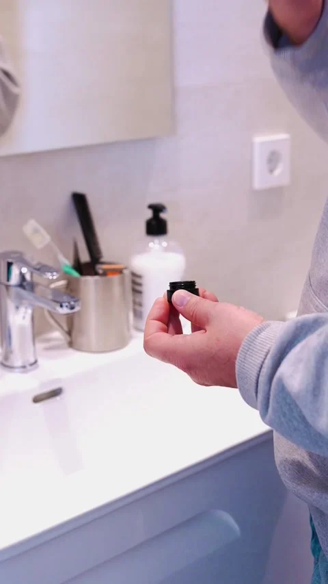 A middle aged man applying beauty cream to his face in front of a mirror Stock Footage 302026740