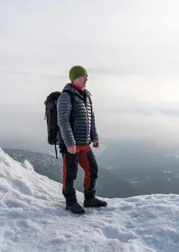 A middle-aged man with a backpack stands on the edge of a mountain. Winter view Stock Photos