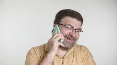 A middle-aged man with a beard and glasses is happily talking on a smartphone Stock Footage 156083747