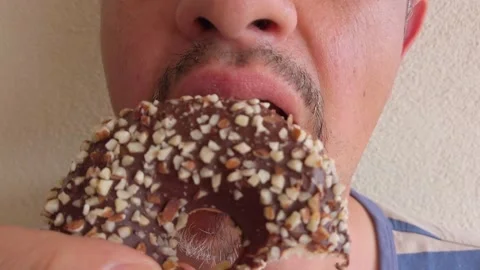Middle-aged man with beard eats donut with chocolate icing. Portrait. Close-up. Stock Footage 133601063
