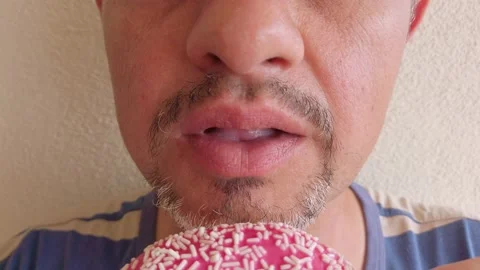 Middle-aged man with beard eats donut with pink sugar glaze. Portrait. Close-up Stock Footage 133601400