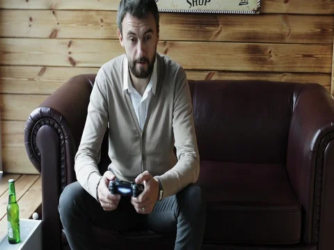 Middle aged man with a beard is holding a remote controller and playing a video Stock Footage 80066982