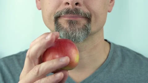 Middle aged man with beard holds in hand and eats heathy red apple, close up 4K Stock Footage 157456301