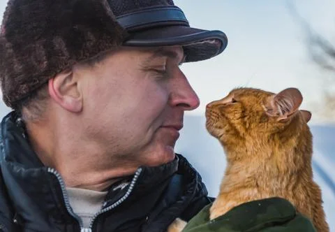 A middle-aged man in a brown hat and a red cat look at each other in winter Stock Photos