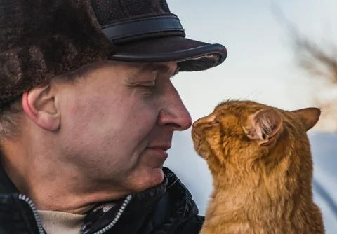 A middle-aged man in a brown hat and a red cat look at each other in winter 스톡 사진