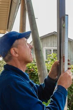 A middle-aged man builder in a blue jacket and blue cap places a black iron p Stock Photos