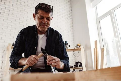 Middle-aged man carpenter working in a workshop with chisel and hammer Stock Photos