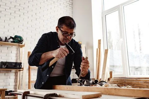 Middle-aged man carpenter working in a workshop with chisel and hammer Stock Photos