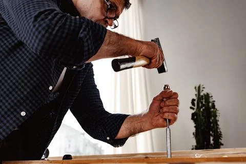 Middle-aged man carpenter working in a workshop with chisel and hammer Stock Photos