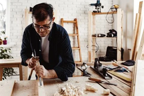 Middle-aged man carpenter working in a workshop with chisel and hammer Stock Photos